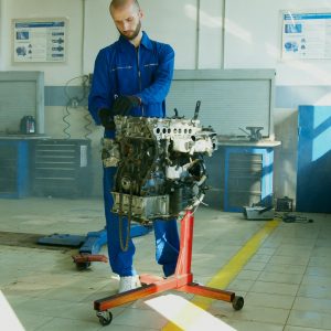 Mechanic in blue overalls inspecting an engine inside a workshop, focused on automotive diagnostics and repair.