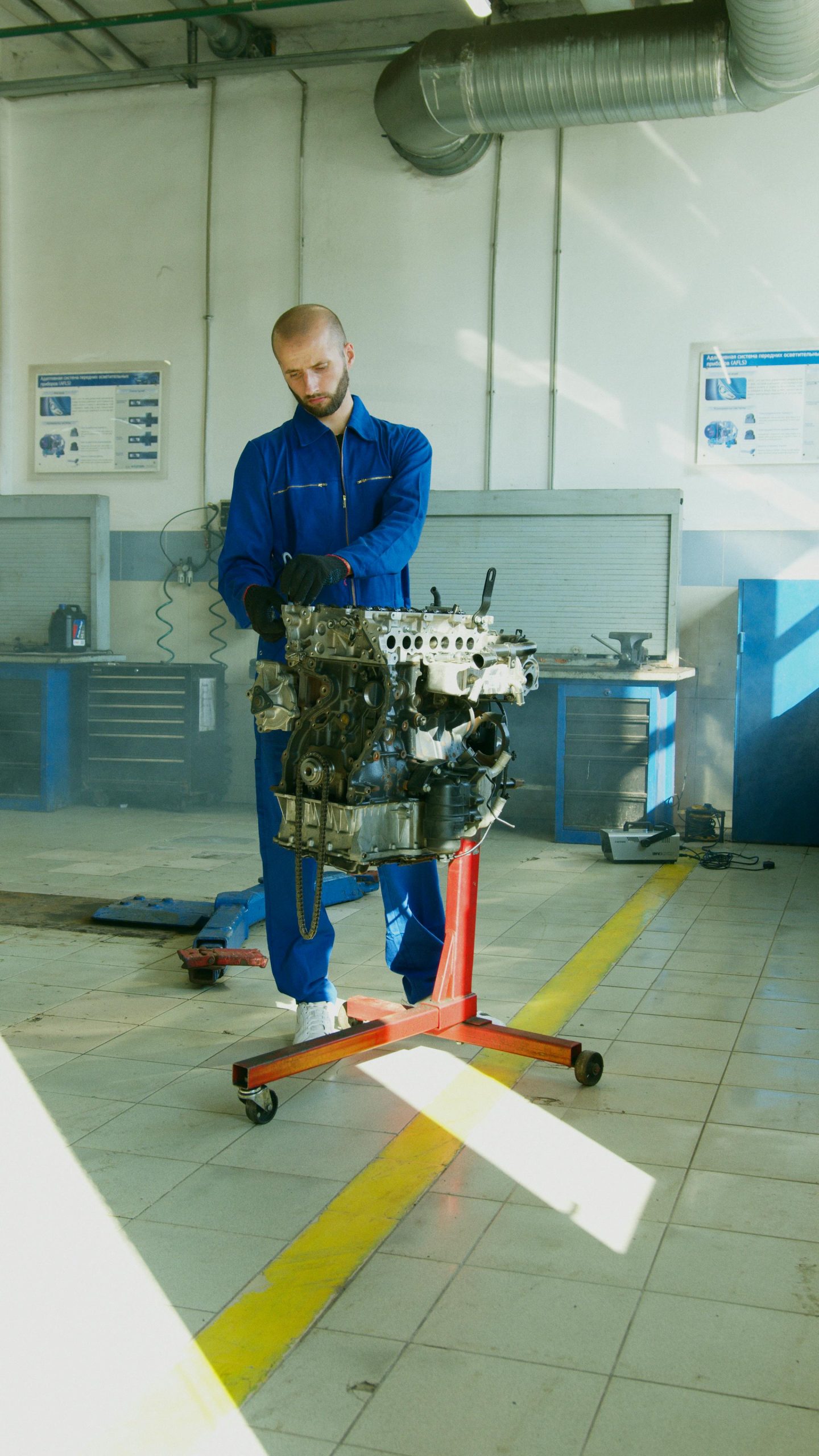 Mechanic in blue overalls inspecting an engine inside a workshop, focused on automotive diagnostics and repair.