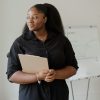 A professional woman stands with a clipboard, exuding confidence in an office setting.