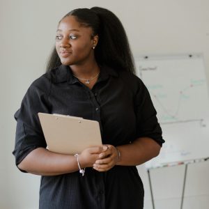 A professional woman stands with a clipboard, exuding confidence in an office setting.