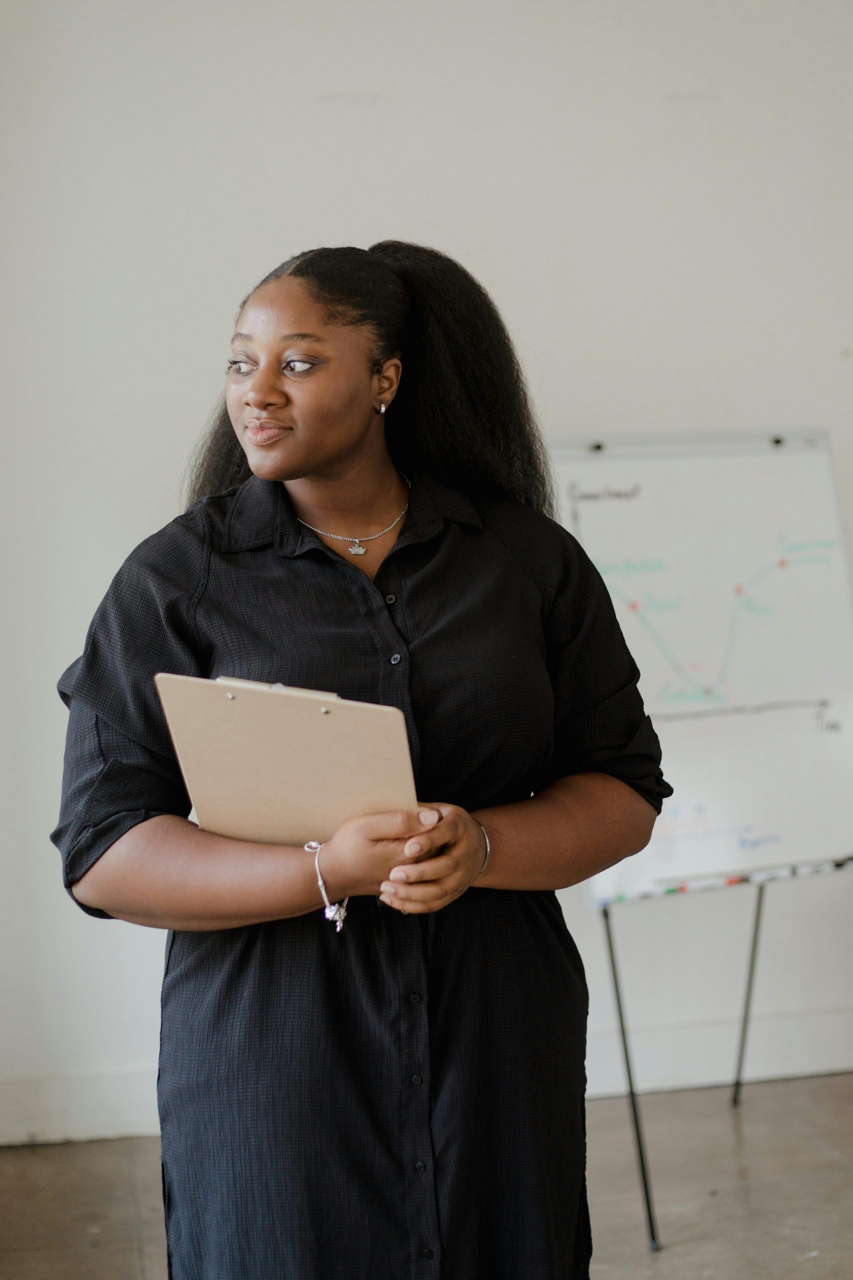 A professional woman stands with a clipboard, exuding confidence in an office setting.